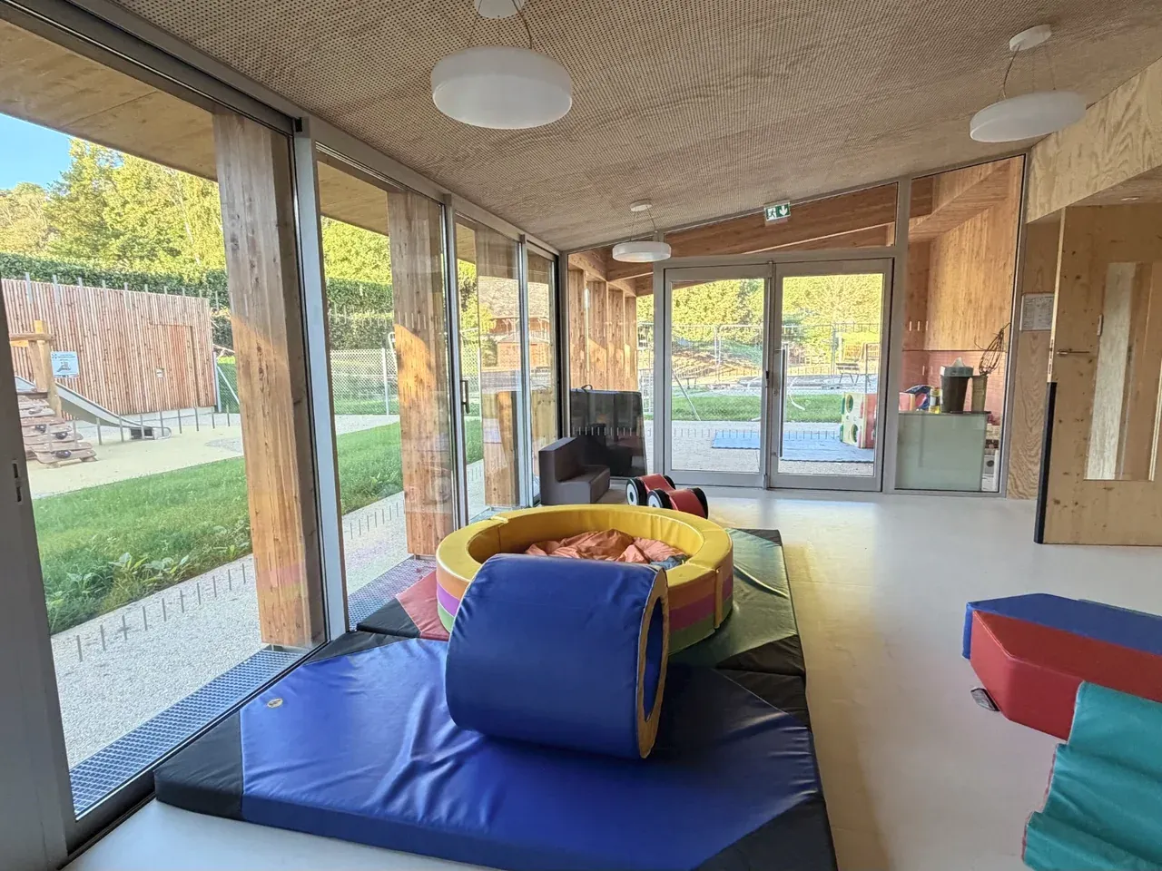 Espace de motricité de la crèche avec tapis colorés, modules en mousse et vue sur le jardin.